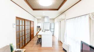 横向きのキッチン。リビングの中心に白いペニンシュラ型のキッチンを置いた事例。