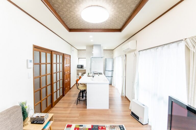 横向きのキッチン。リビングの中心に白いペニンシュラ型のキッチンを置いた事例。